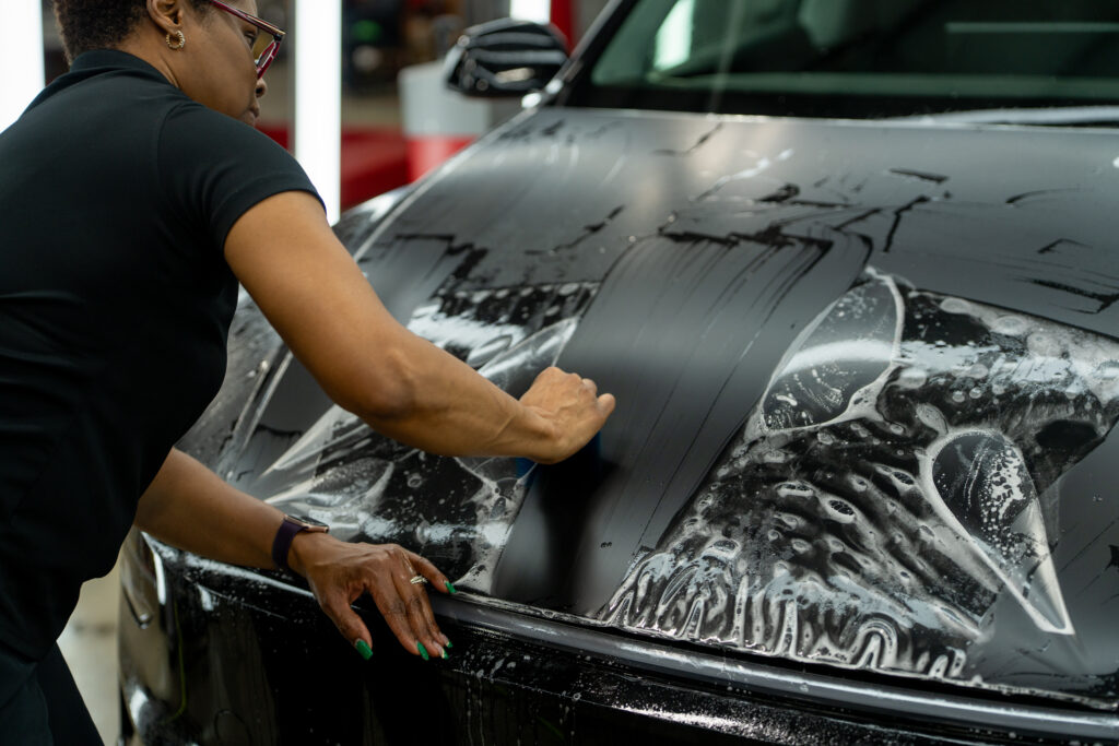 Installer applying XPEL Stealth paint protection film to the hood of a black 2026 Tesla Model Y, installed by Exclusive Paint Protection