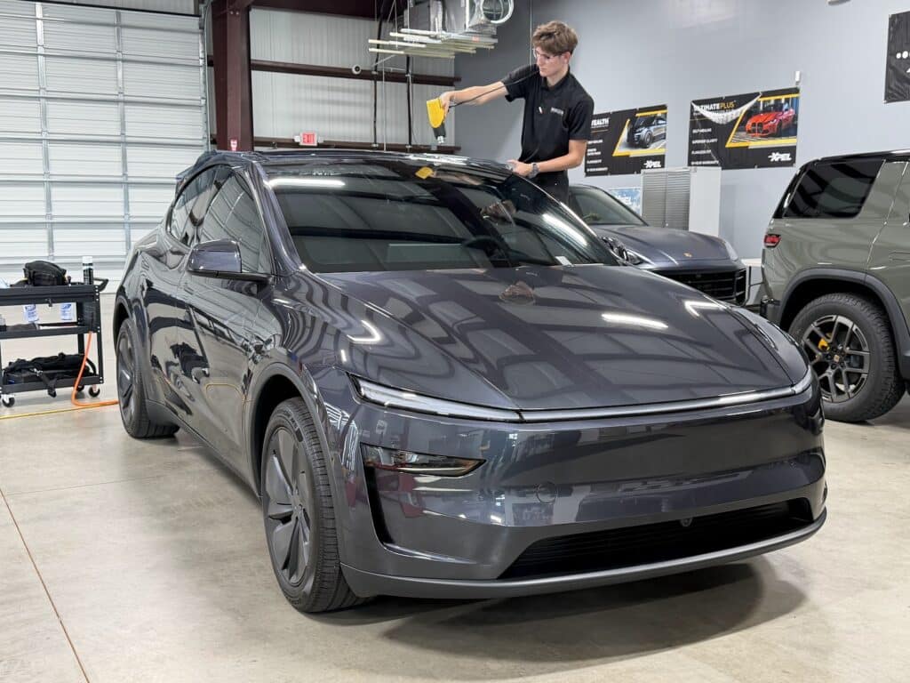 EPP installer heat-forming XPEL window tint film on a new Tesla Model Y at our studio, with a Porsche and Rivian in the next bays