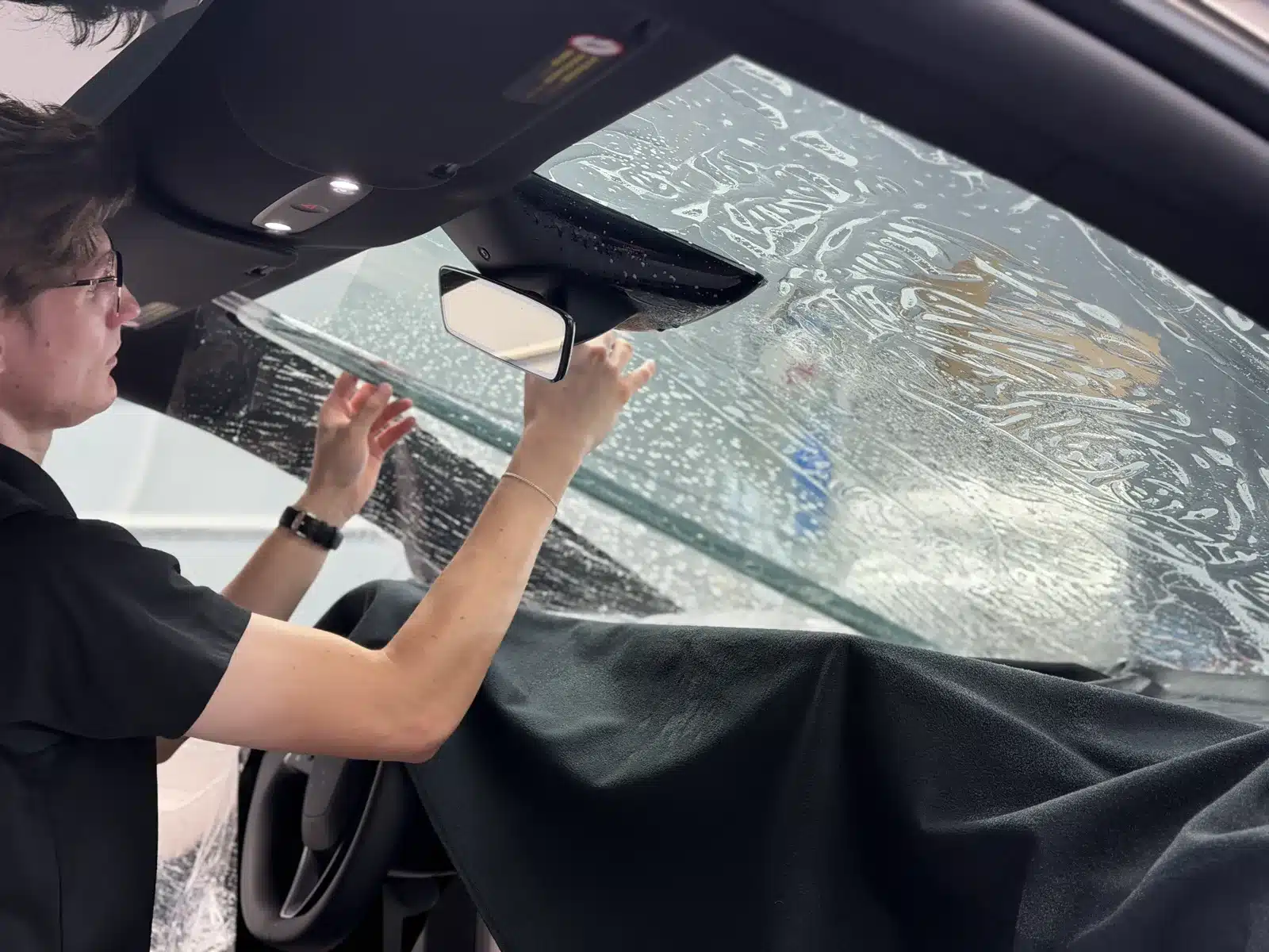 EPP installer applying 70% XPEL PRIME XR PLUS ceramic window tint to the inside of the windshield of the silver Tesla Model Y L at Exclusive Paint Protection's Charlotte studio