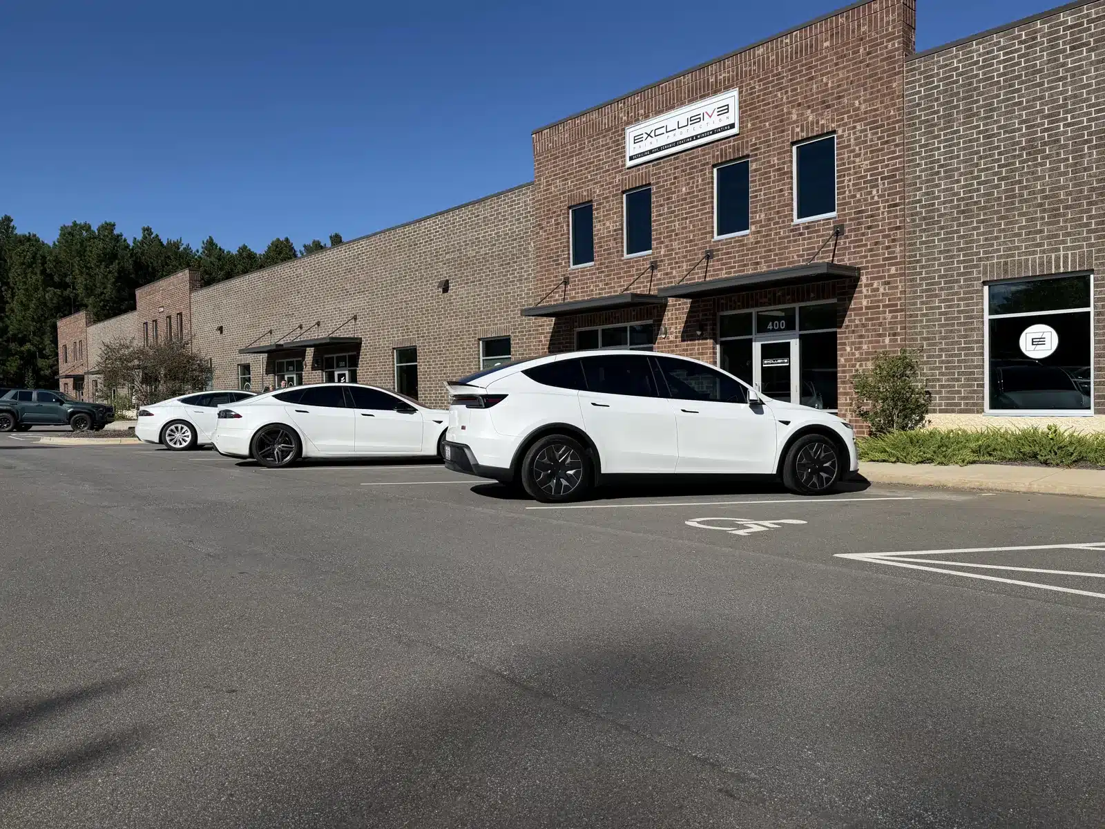White Tesla Model Y L with XPEL PRIME XR PLUS ceramic window tint parked outside Exclusive Paint Protection's Huntersville studio on Reese Blvd